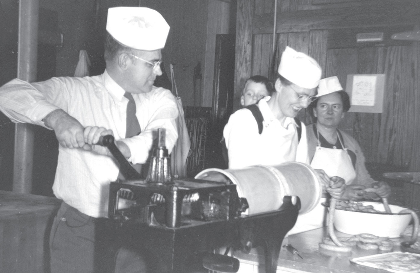 Nueske's Eddie Schwartz grinds sausage with Aunts' Elda and Irma stuffing casings. Young Bob Nueske is peeking to watch the process. Circa 1957. Contributed photo.